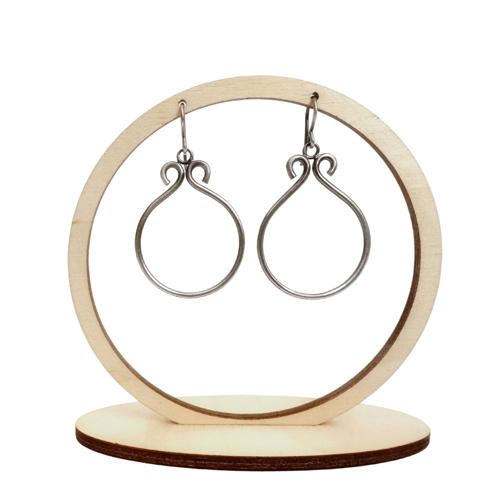 A set of sterling silver hoop earrings hanging from a wooden earring holder, in front of a white background. The hoops have been oxidised.