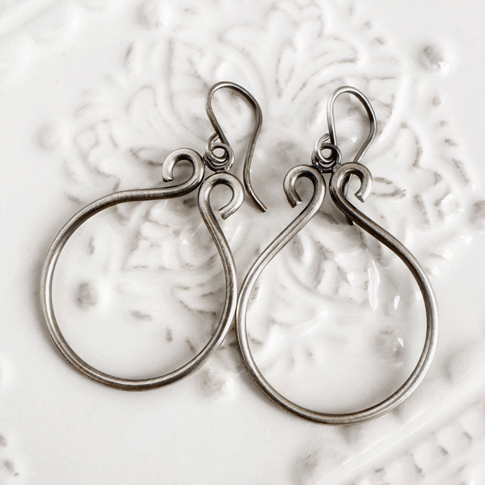 A set of sterling silver hoop earrings on  a white background. The hoops have been oxidised.