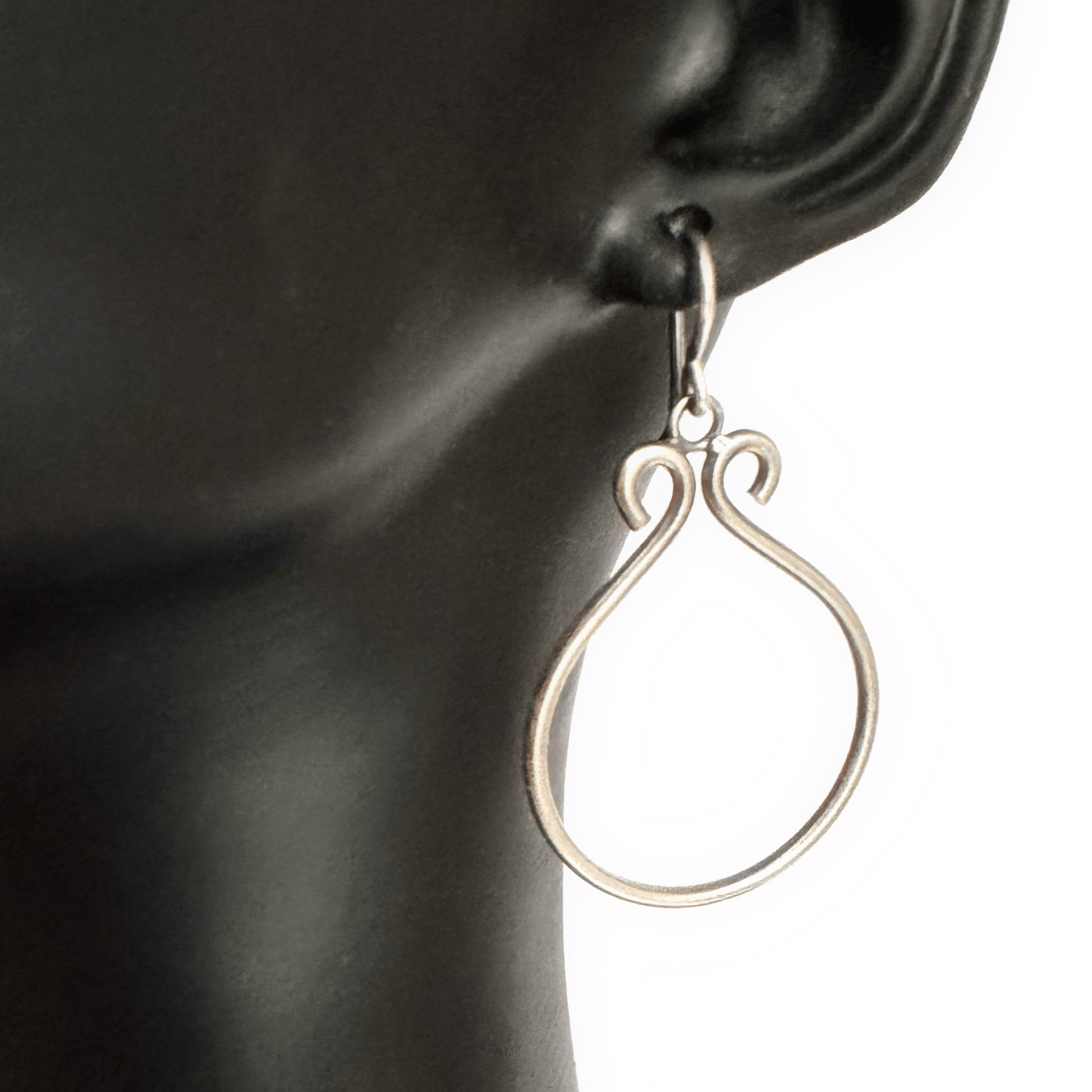 Sterling silver hoop earring hanging from a black mannequin ear in front of a white background. The hoop has been oxidised.